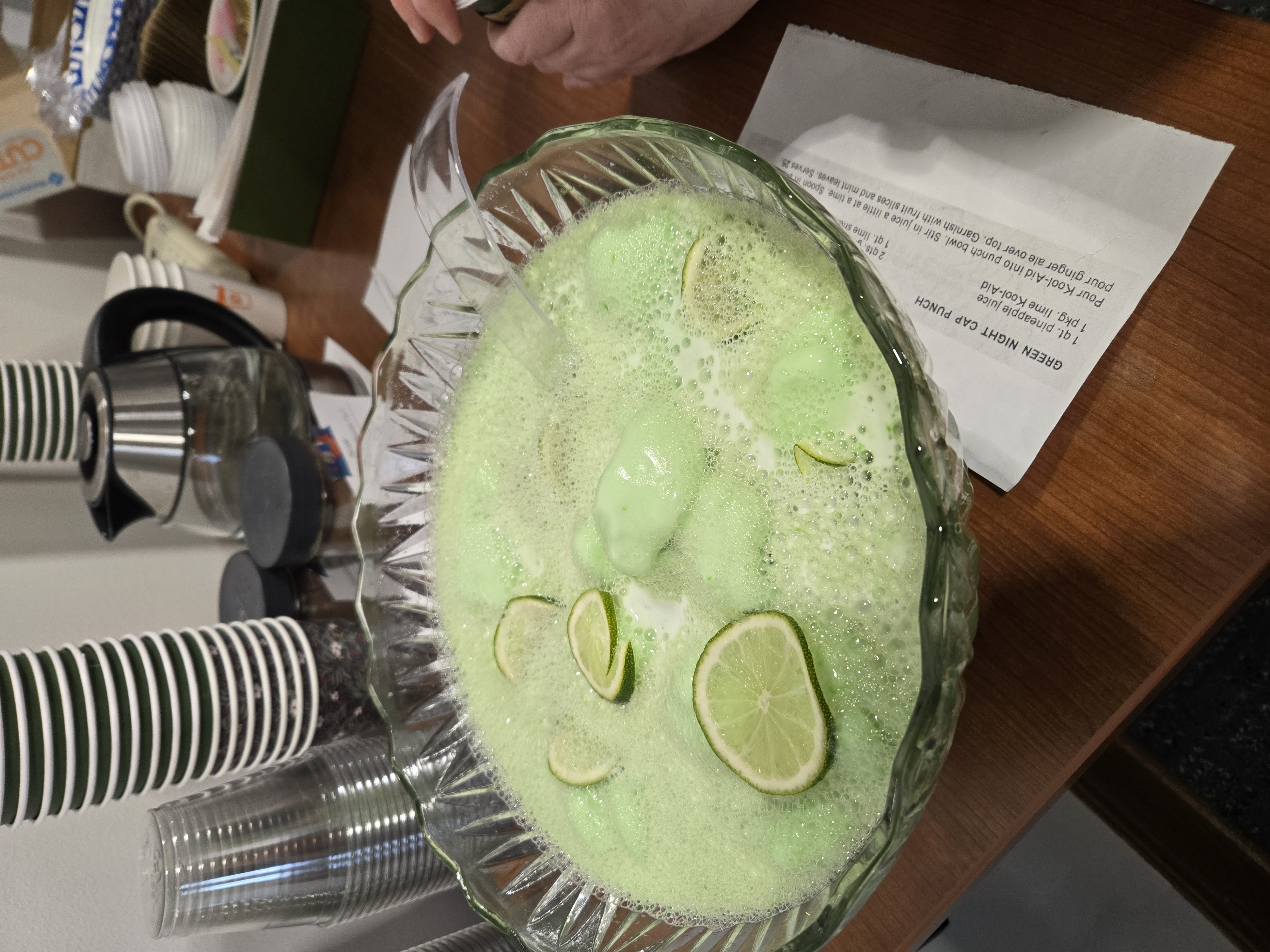 A large glass bowl of green punch with lime slices.
